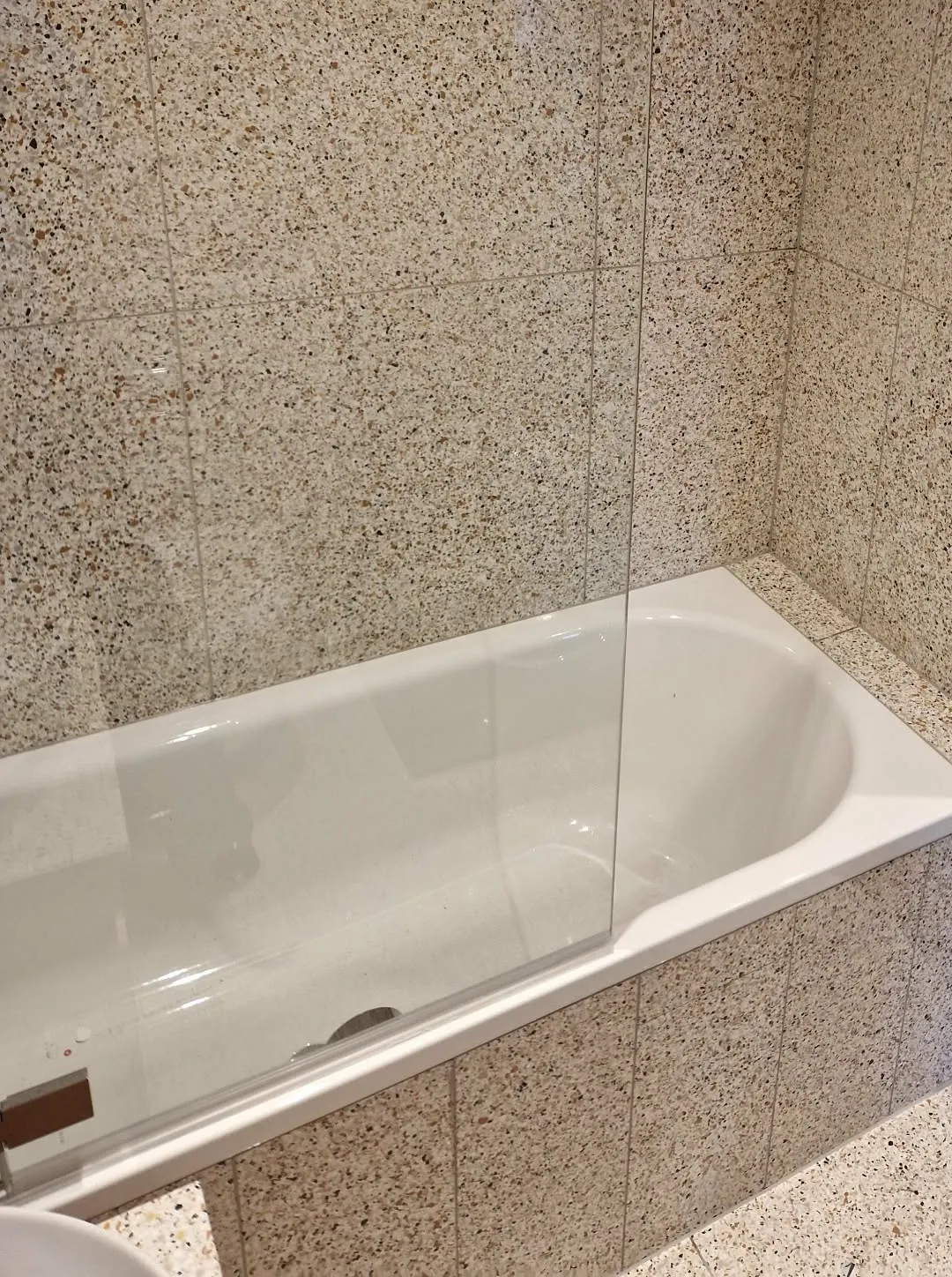 Bath with terrazzo-effect tiles on the walls and bath panel, and a glass bath screen
