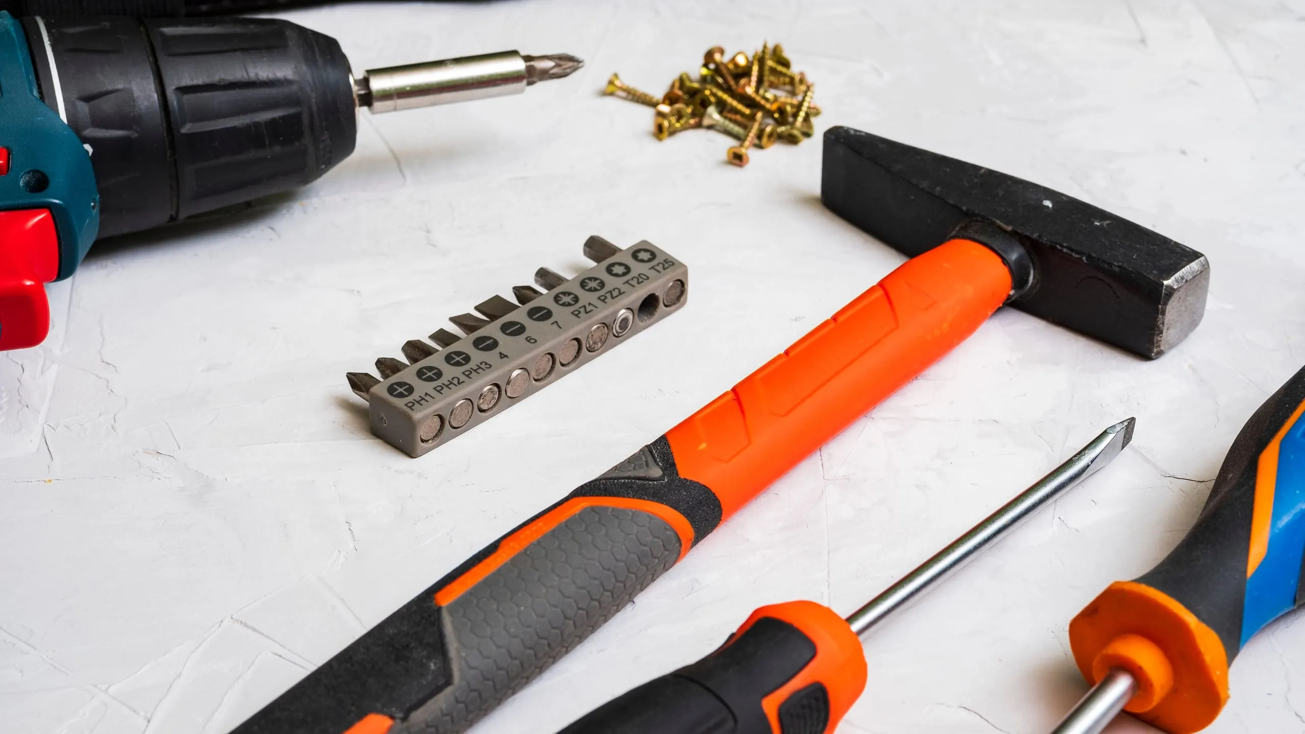 Hammer, screwdriver and drill bits on a white plastered surface
